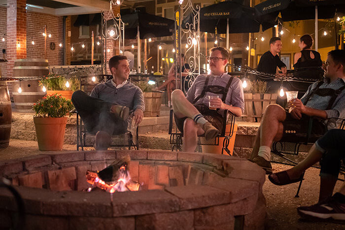 People sitting around a fire pit in an outdoor patio setting. Several men are wearing authentic German lederhosen.
